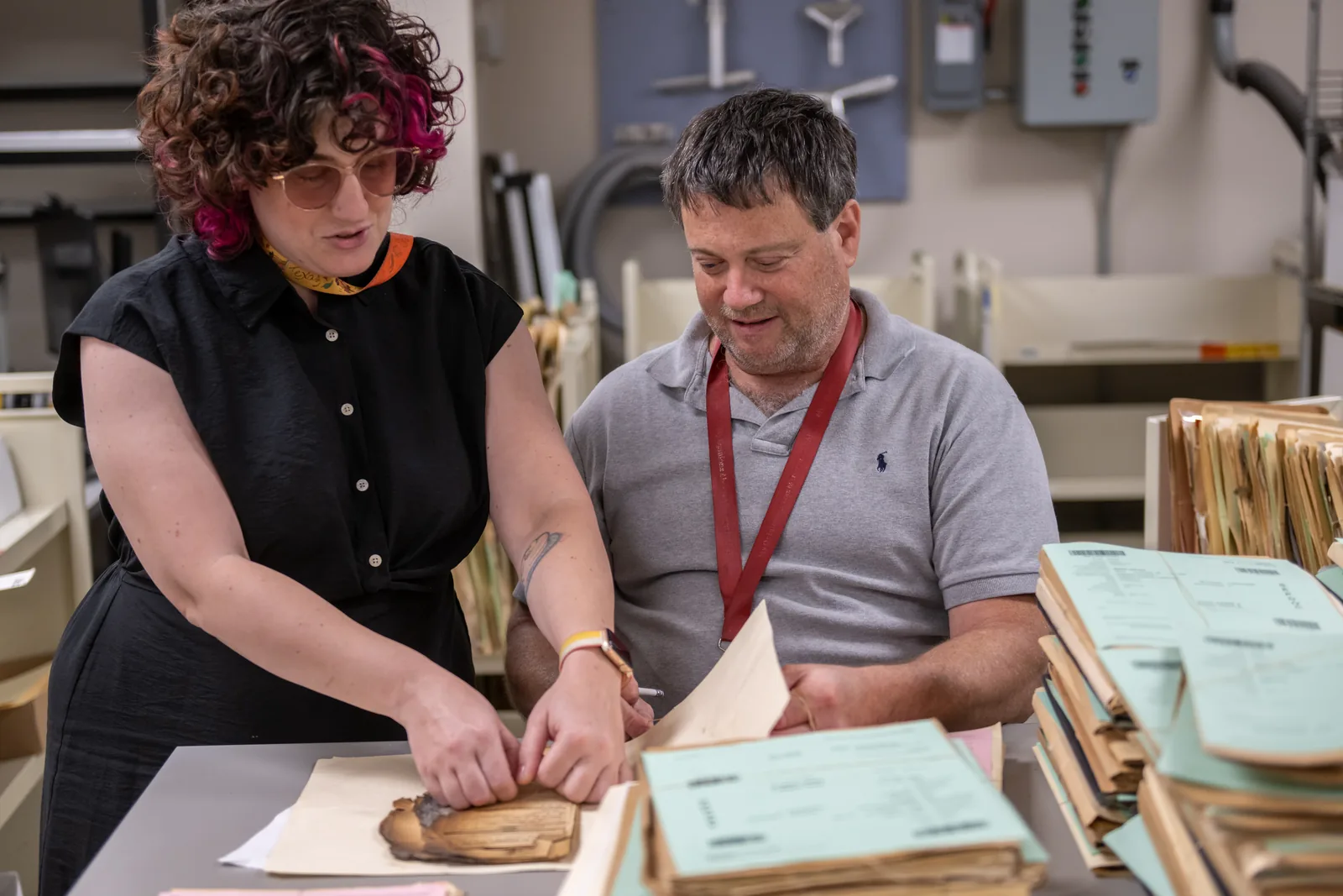 Two National Archives preservation staff carefully handle a fire-damaged military service file, surrounded by records.